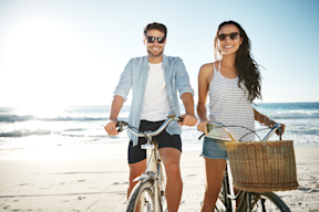 Couple riding bikes on the beach smiling wearing prescription sunglasses uv protection